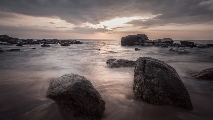 Eine felsige Küste mit großen Felsen und ruhigem Meer unter einem bewölkten Himmel.