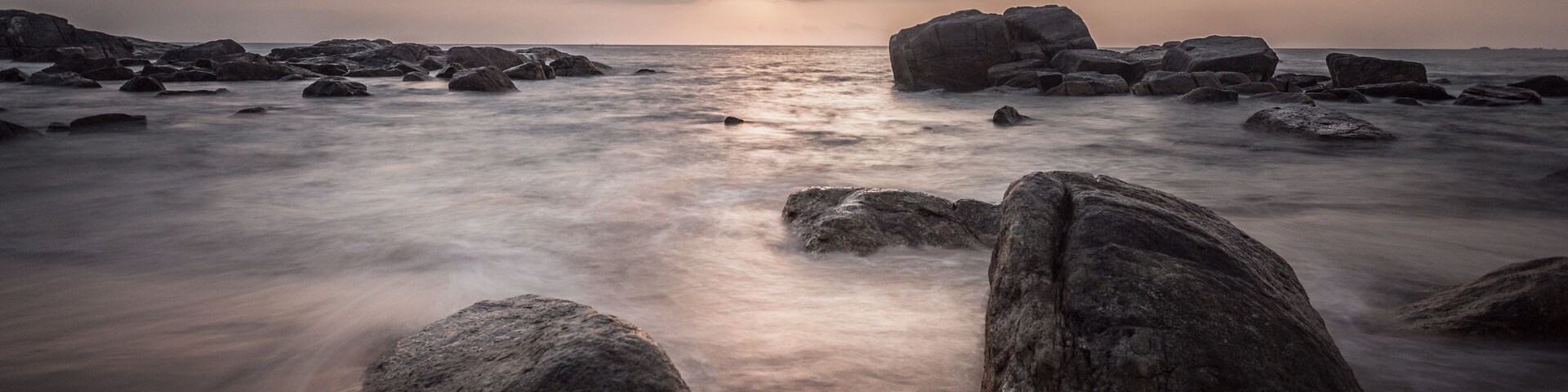 Una costa rocosa con grandes rocas y un mar tranquilo bajo un cielo nublado.