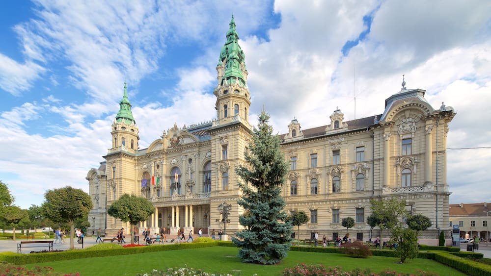 A grand historic building with ornate architecture, including two prominent towers and a well-maintained garden.