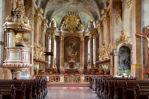An ornate church interior with a central altar, rows of pews, and elaborate gold decorations.