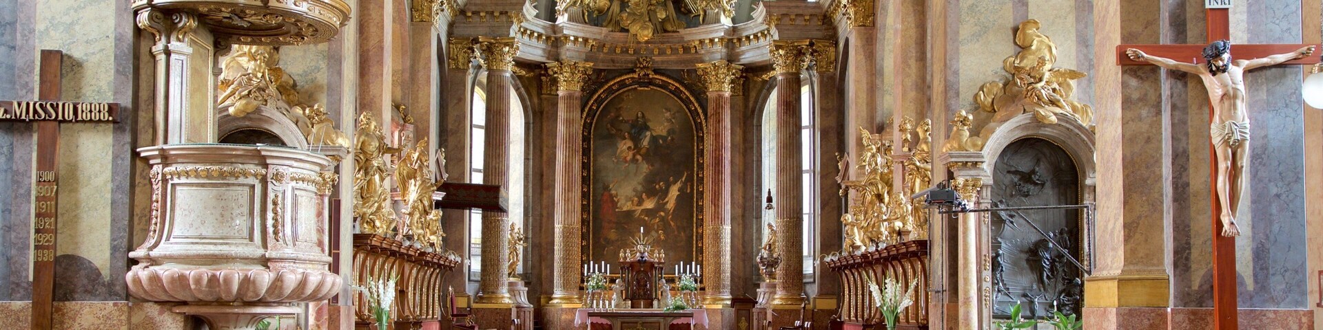 Interior de igreja ornamentado, com altar central, fileiras de bancos e elaboradas decorações em dourado.