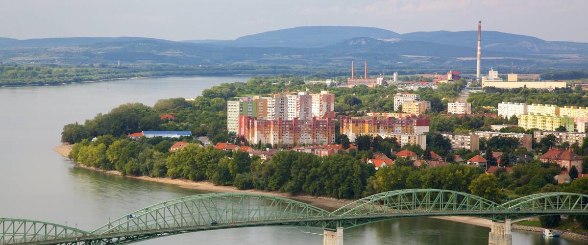 A green bridge over a river, a cityscape with colorful buildings, and a distant mountain range.