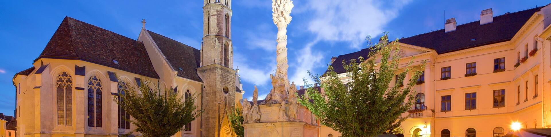 A historic square with a tall church tower, a statue, and traditional buildings.