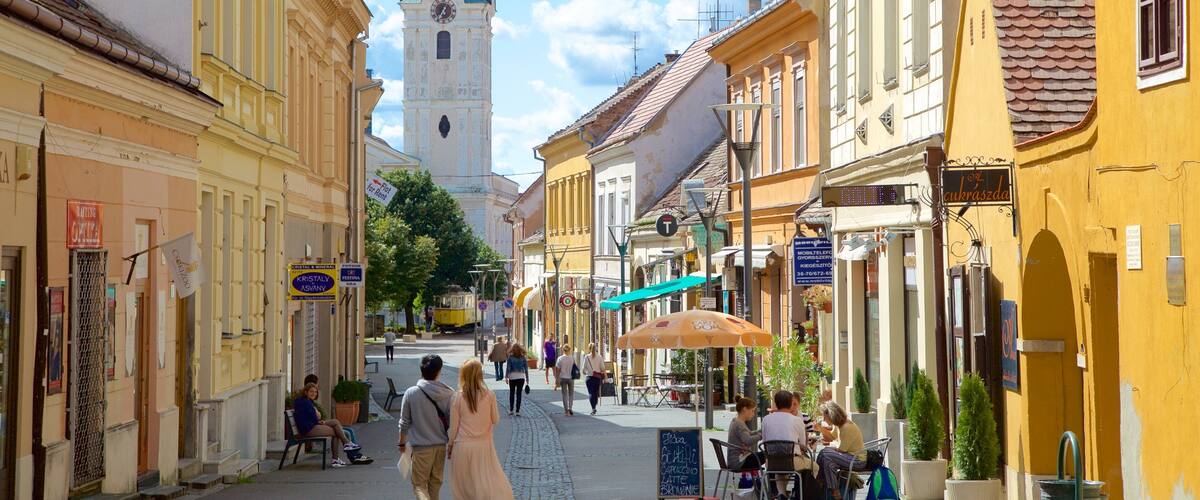 A street with yellow buildings, a church with a tall spire, and people walking.