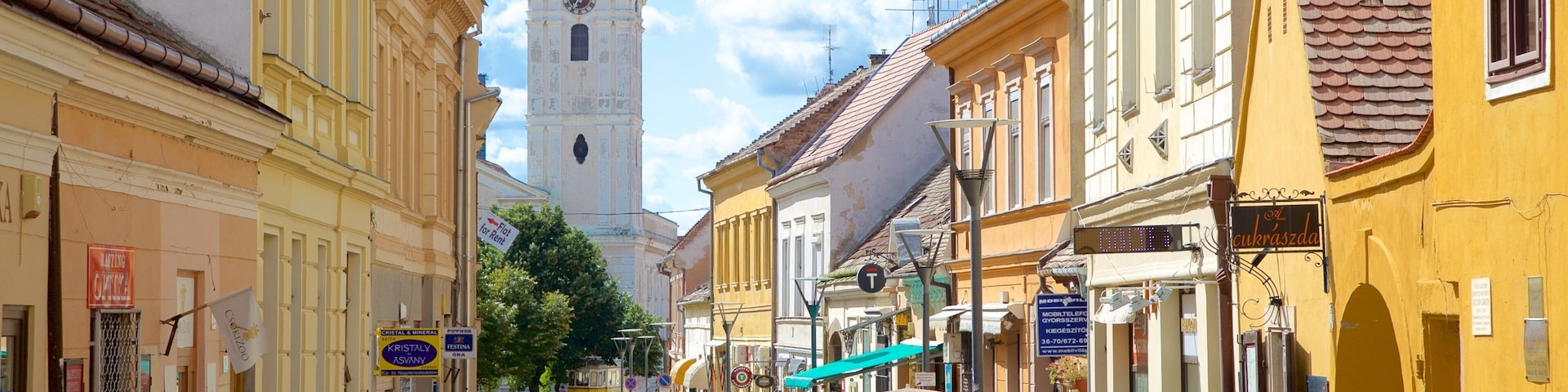 A street with yellow buildings, a church with a tall spire, and people walking.