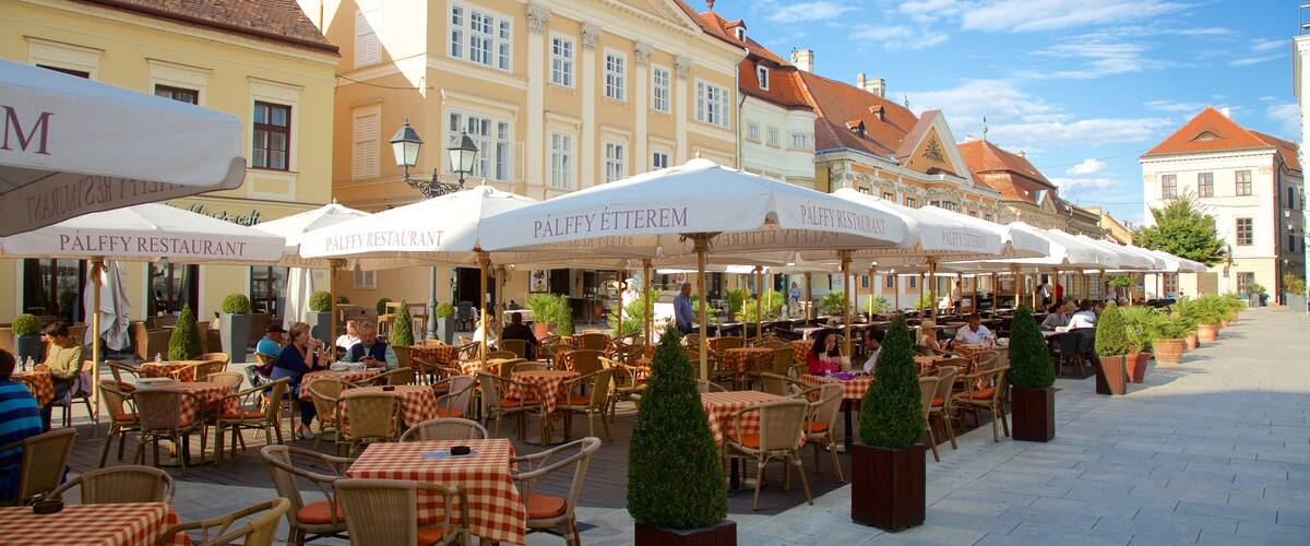 Outdoor café tables and chairs with umbrellas, a building with a red roof, and a clear blue sky.