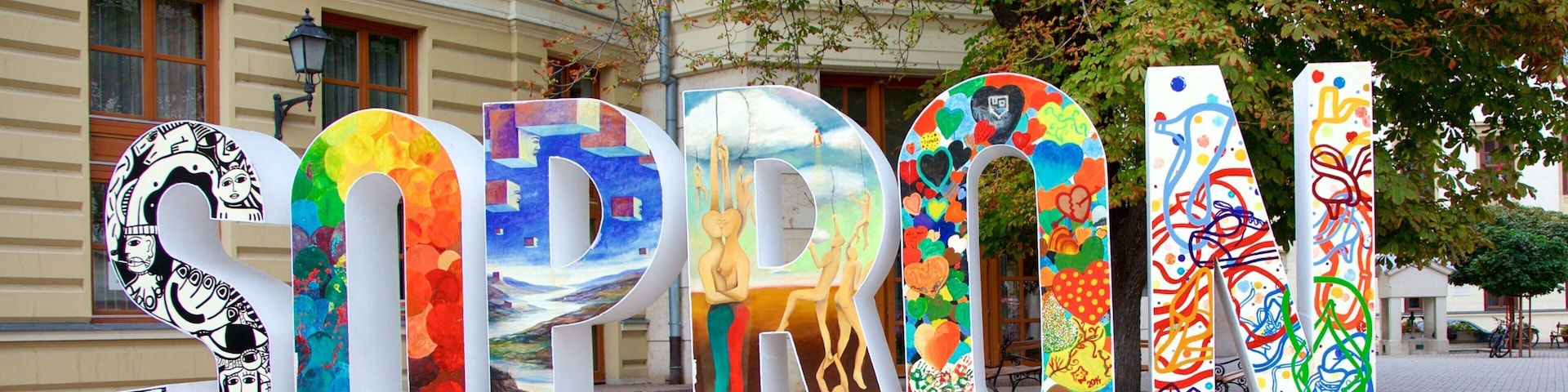 Grandes letras coloridas que deletrean 'SOPRON' sobre una superficie pavimentada.