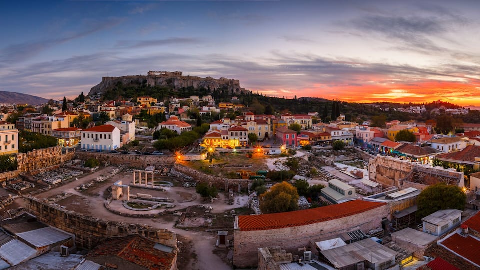 A historic town with ancient ruins, a prominent castle on a hill, and a sunset sky.