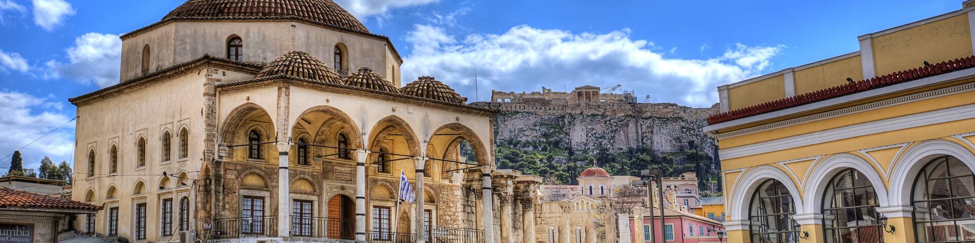 A historic building with a dome and arches, a fortification on a hill, and a clear blue sky.
