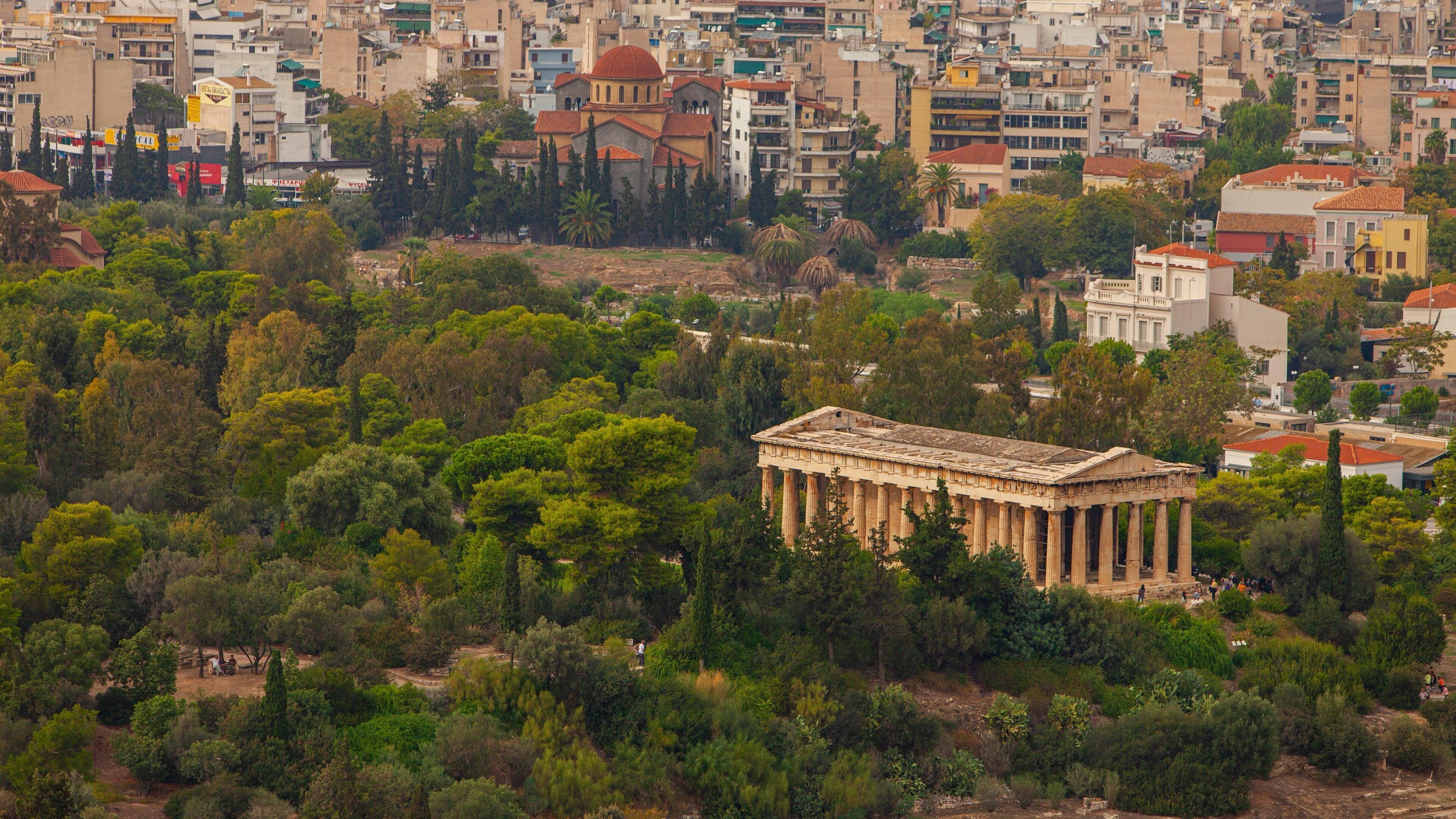 A cityscape with a prominent ancient Greek temple surrounded by dense greenery.