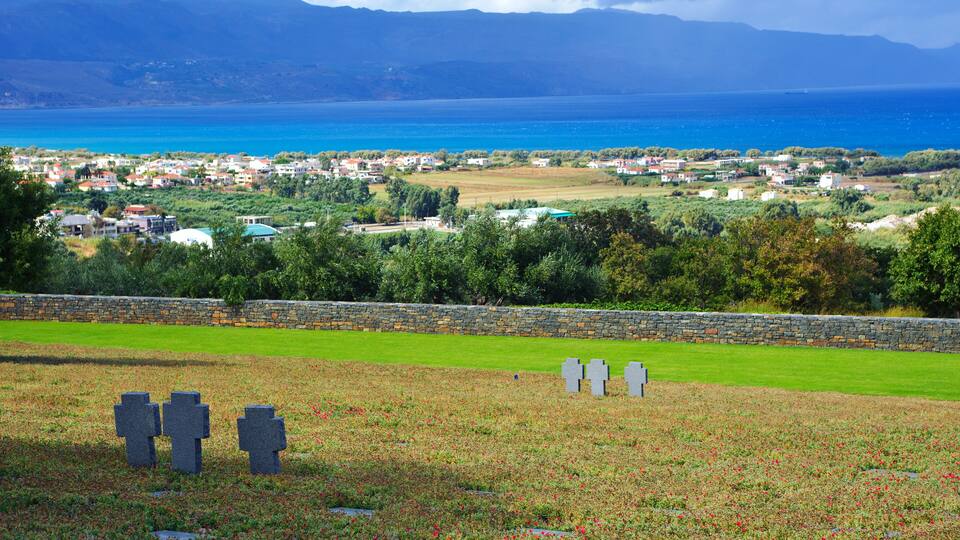 A coastal town with a cemetery, stone wall, and mountains in the background.