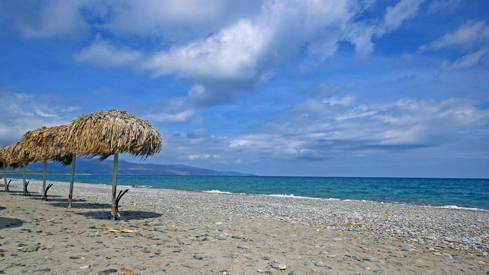 A beach with a thatched umbrella and pebbles.
