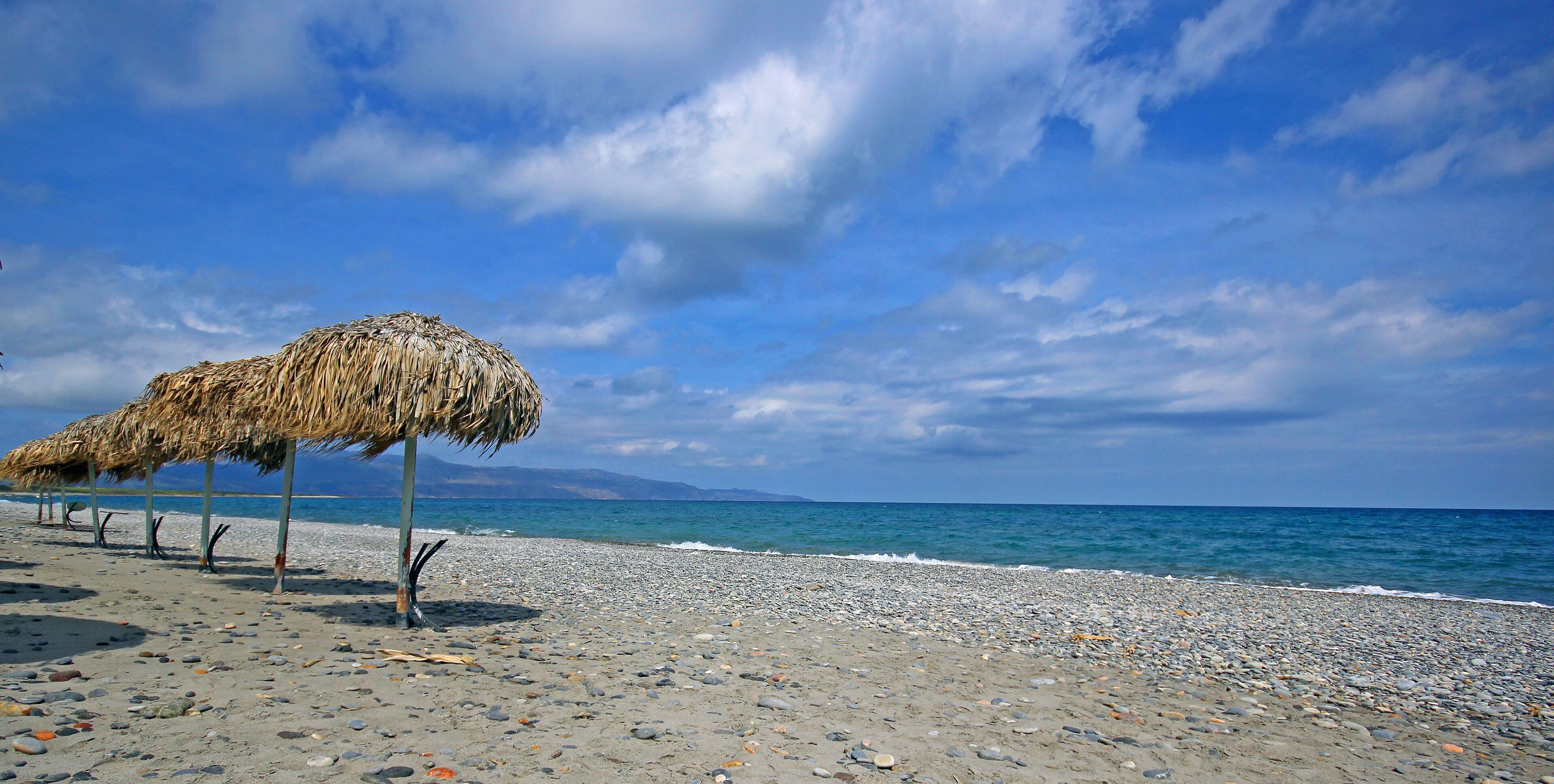 A beach with a thatched umbrella and pebbles.