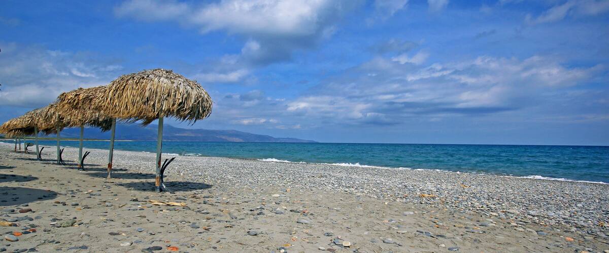 A beach with a thatched umbrella and pebbles.