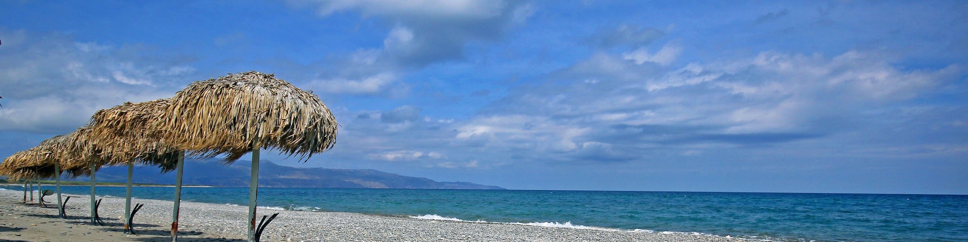 A beach with a thatched umbrella and pebbles.