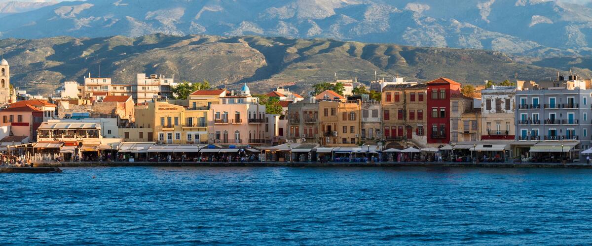 A coastal town with colorful buildings and a mountain range in the background.