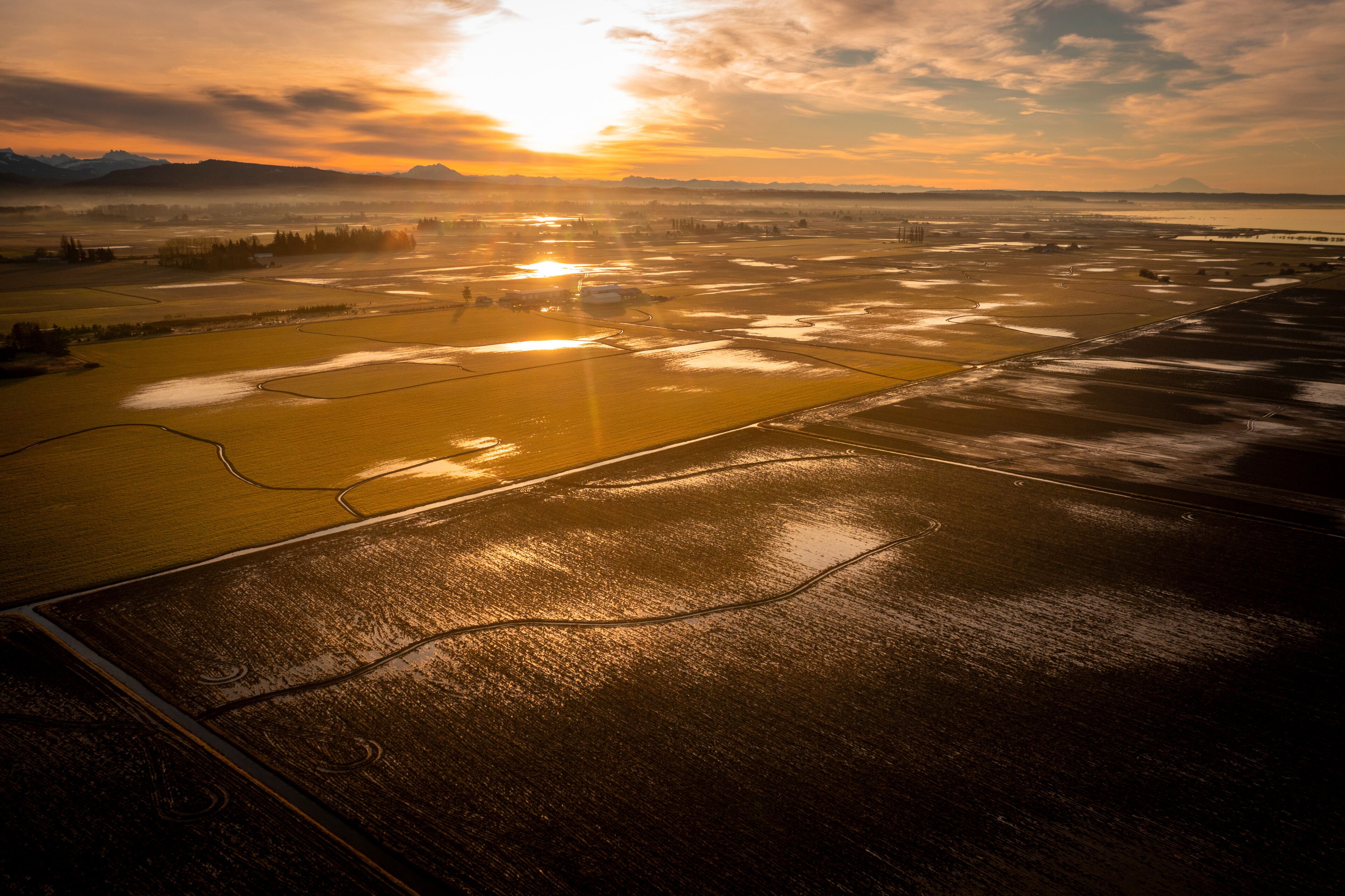 Un paisaje extenso con un río, campos y montañas distantes bajo un cielo al atardecer.