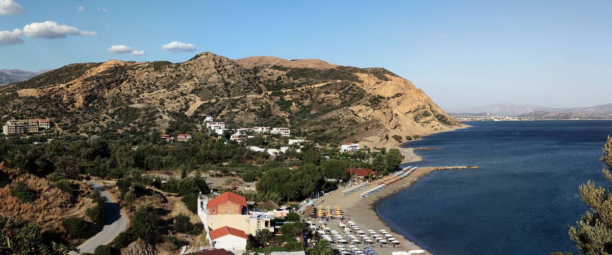 A coastal town with a beach, mountains, and a clear sky.