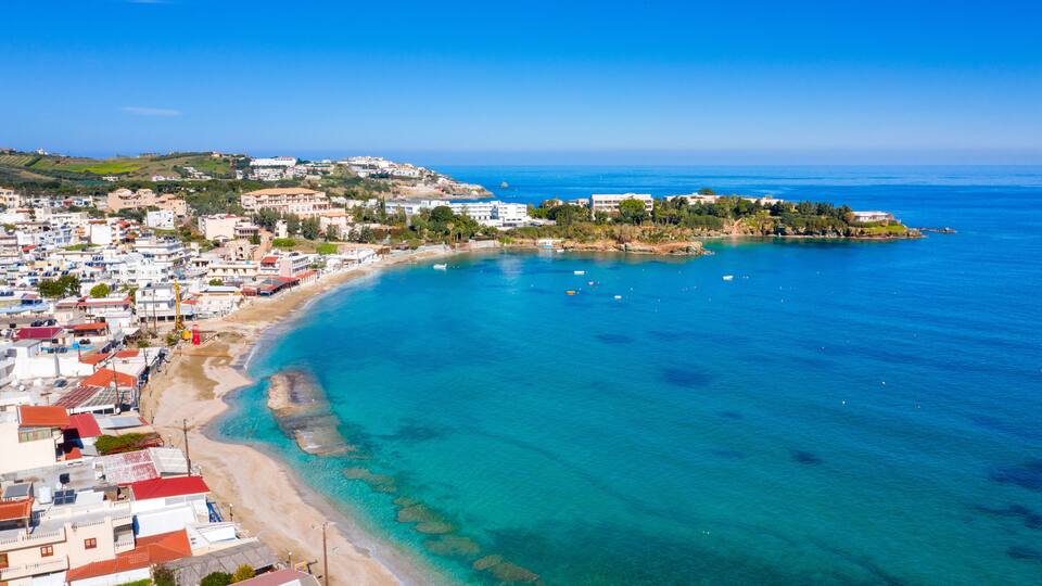 A coastal town with a clear blue sea, sandy beach, and buildings along the shore.