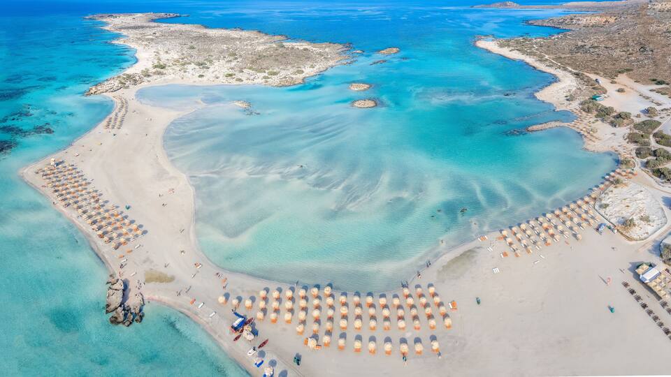 An aerial view of a coastal area with clear turquoise waters, sandy beaches, and a large number of beach umbrellas.