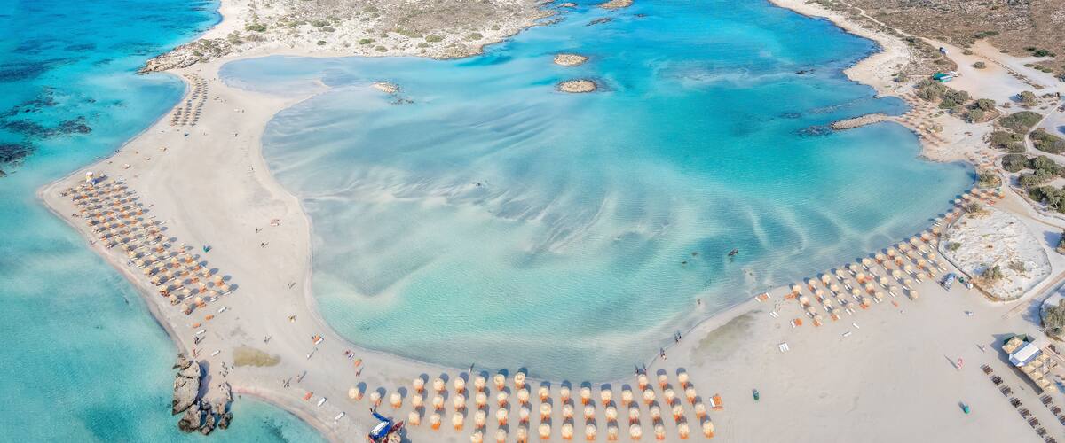 An aerial view of a coastal area with clear turquoise waters, sandy beaches, and a large number of beach umbrellas.