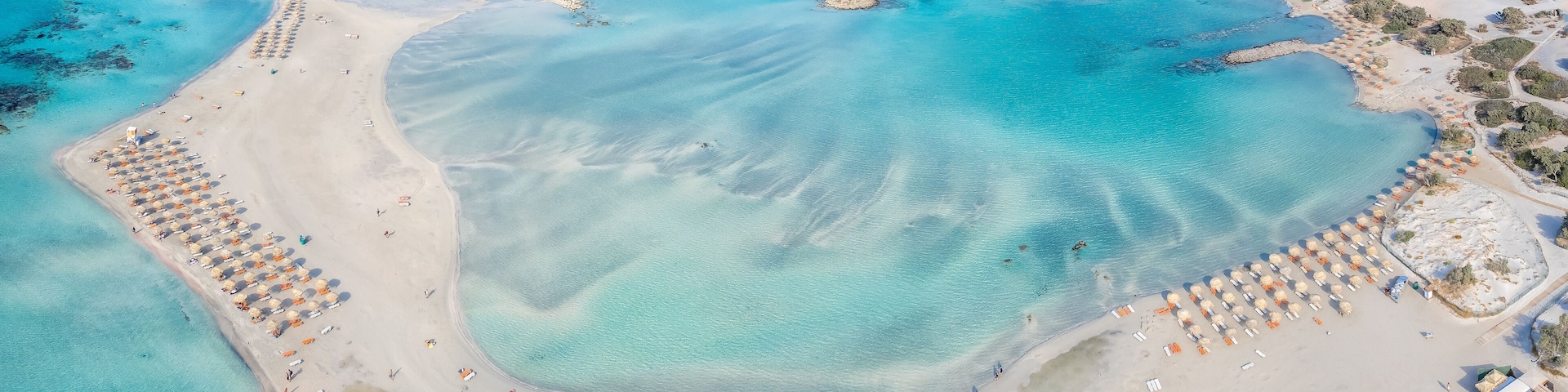 An aerial view of a coastal area with clear turquoise waters, sandy beaches, and a large number of beach umbrellas.