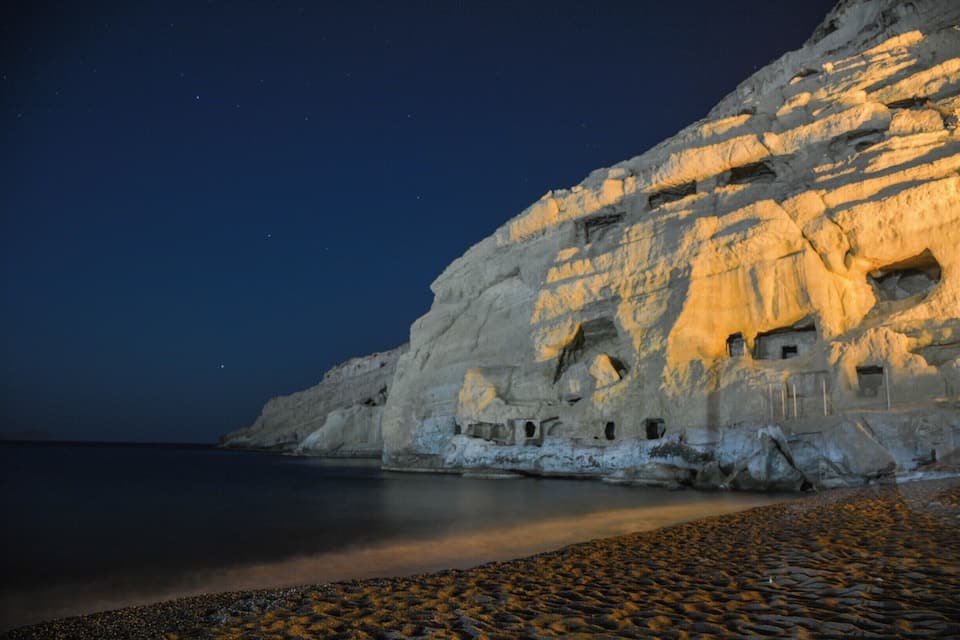 Costa rocosa amb penya-segades blanques i coves il·luminades per llum artificial de nit.
