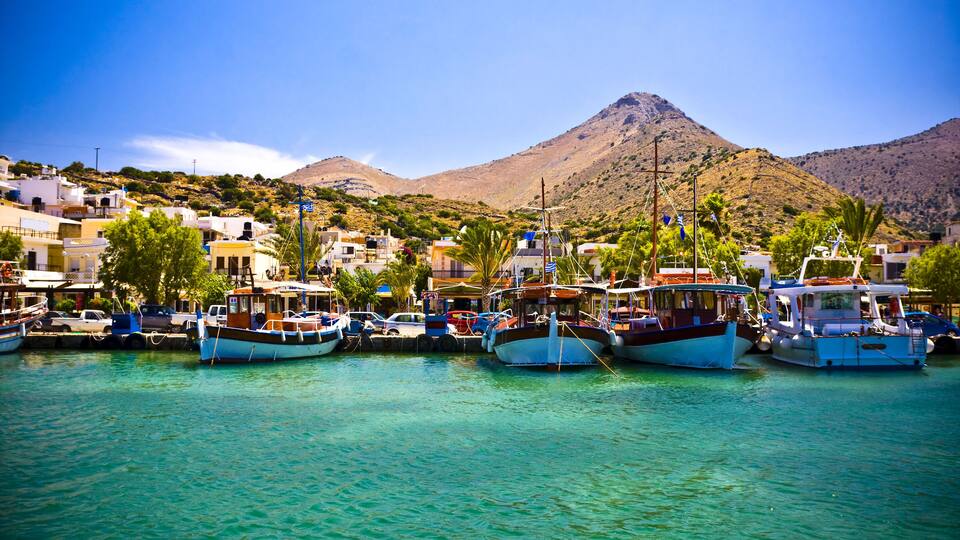 A harbor with boats docked, a mountain in the background, and buildings along the shore.