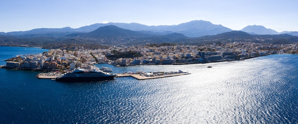 A coastal city with a large cruise ship docked, surrounded by mountains and a clear blue sea.