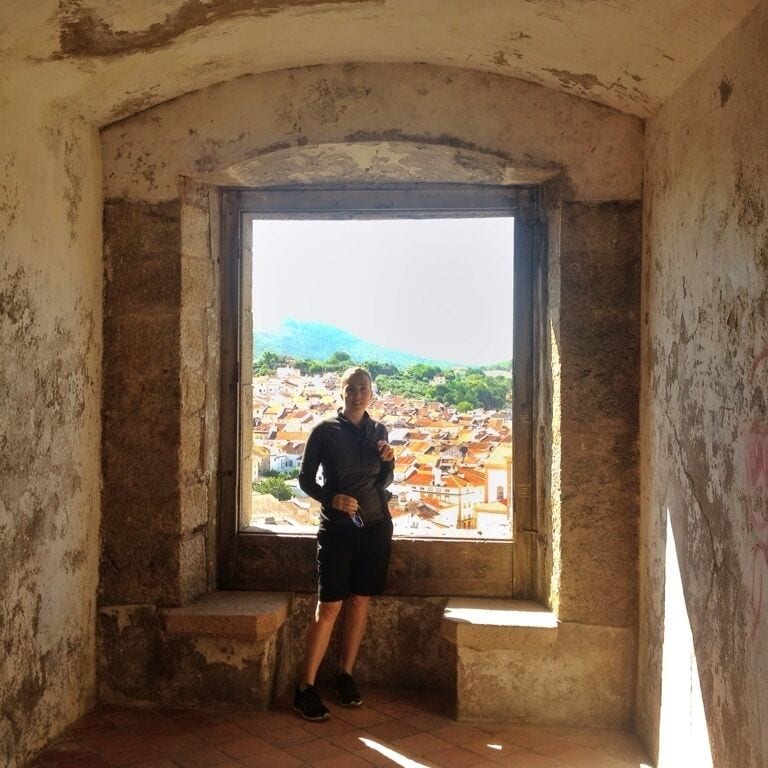 A person standing in a window overlooking a town with buildings and hills in the distance.