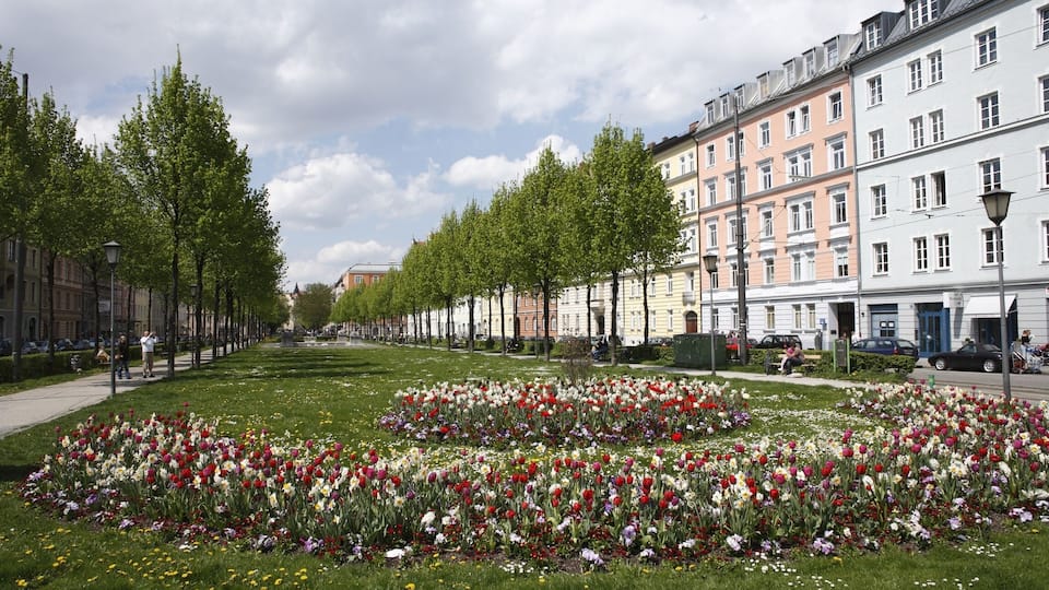 A city street lined with colorful flower beds and historic buildings.
