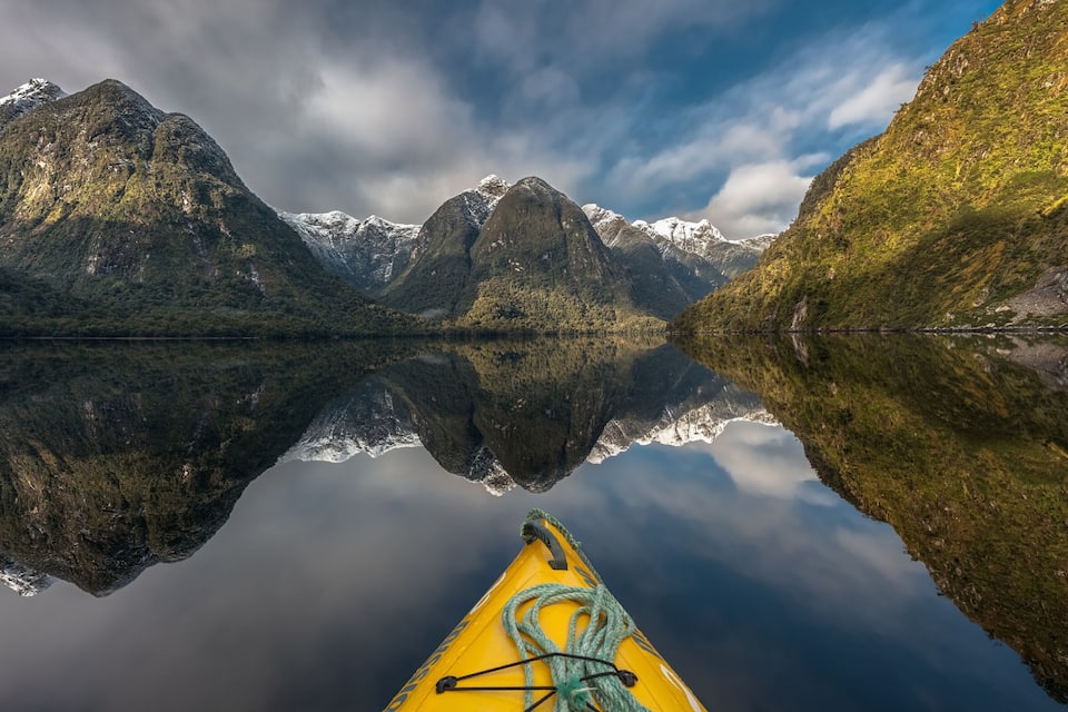 Un kayakiste sur un lac paisible, avec des montagnes en arrière-plan.