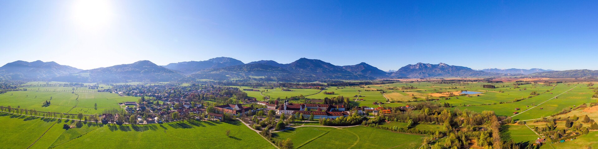 Ein ländliches Dorf mit grünen Feldern, einer Kirche und Bergen im Hintergrund.