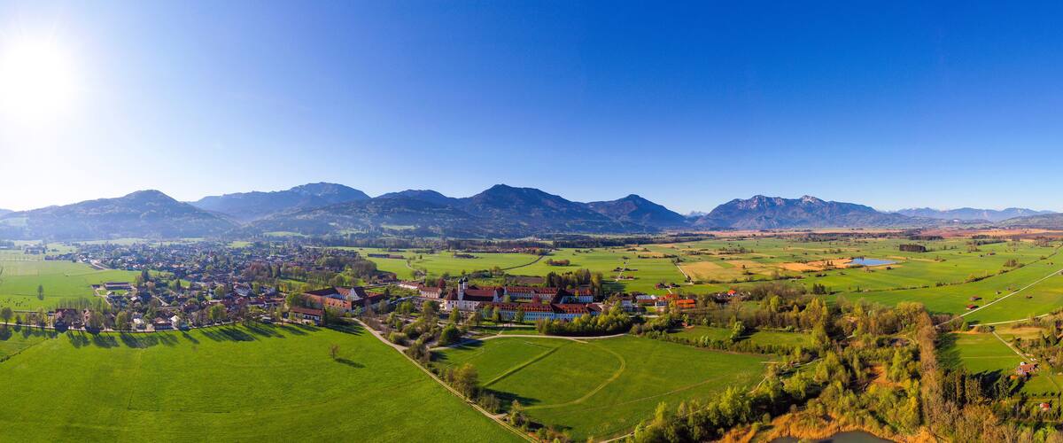 A rural village with green fields, a church, and mountains in the background.