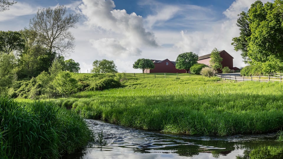 A rural landscape with a river, green fields, and red barns.