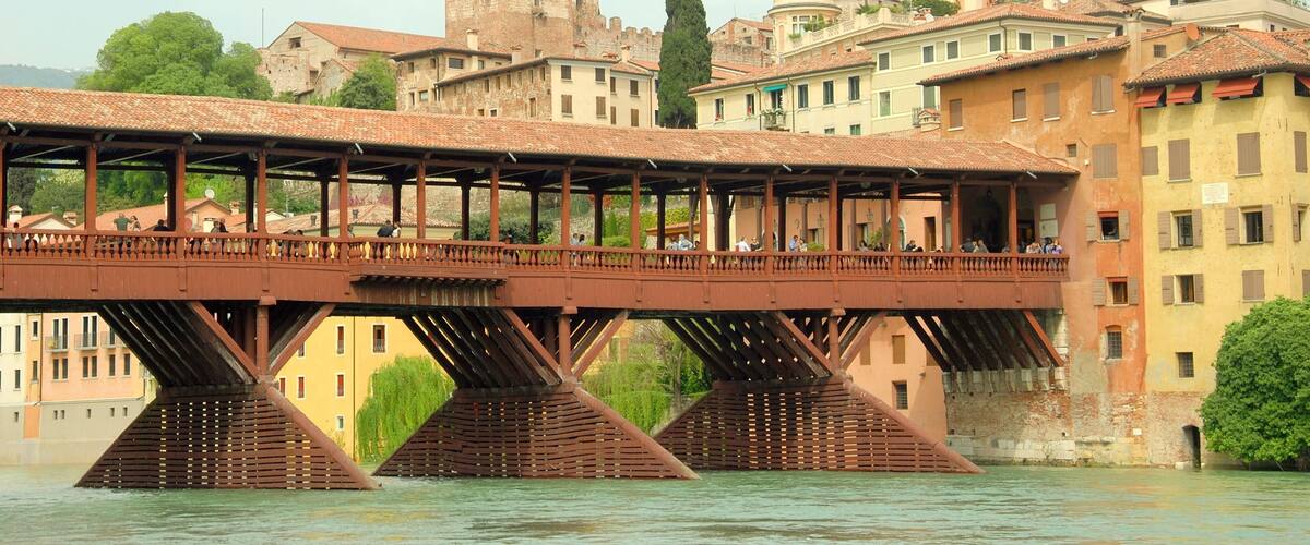 A pedestrian bridge over a river with historic buildings in the background.