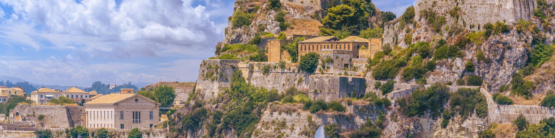 Un pueblo costero con edificios históricos asentados en un acantilado, un faro y un velero en el agua.