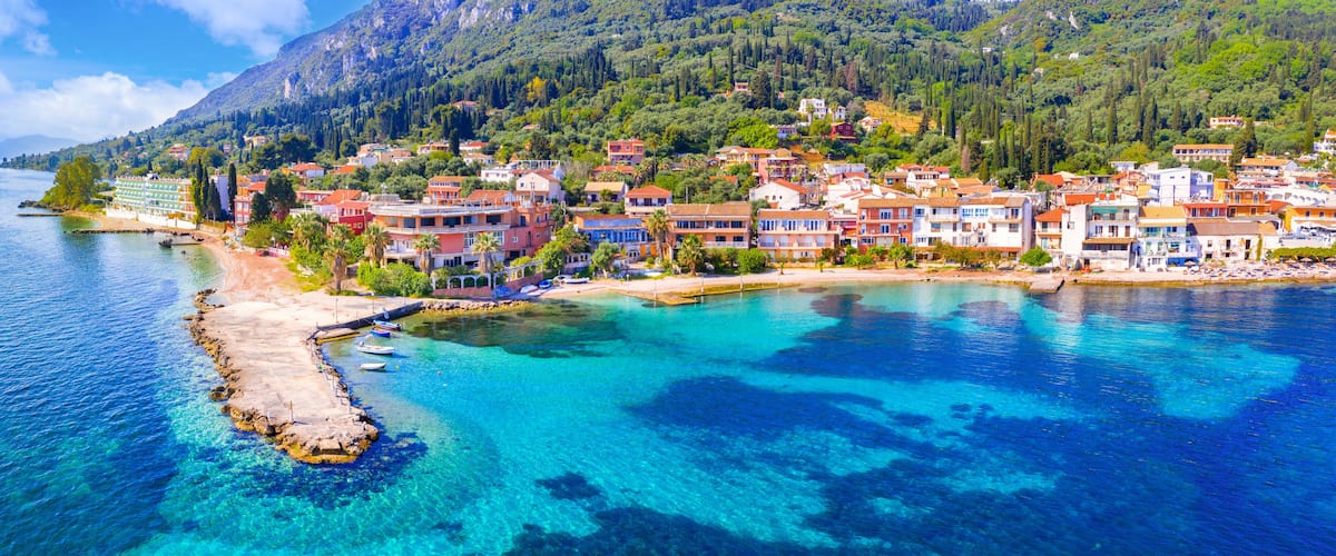 A coastal town with colorful buildings, clear blue waters, and a mountainous backdrop.