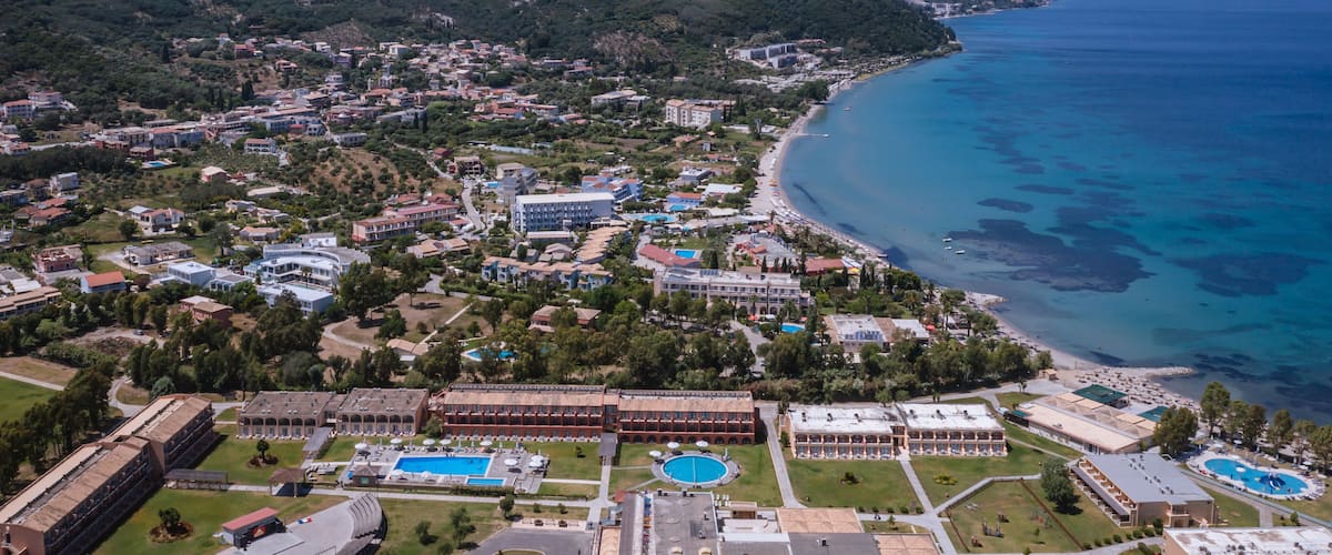 An aerial view of a coastal town with a beach, mountains, and a swimming pool complex.