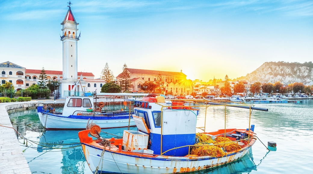 Zante - Zakinthos island, old port with moored boats and church tower landmark. Majestic sunset scenery, sun glowing visible.