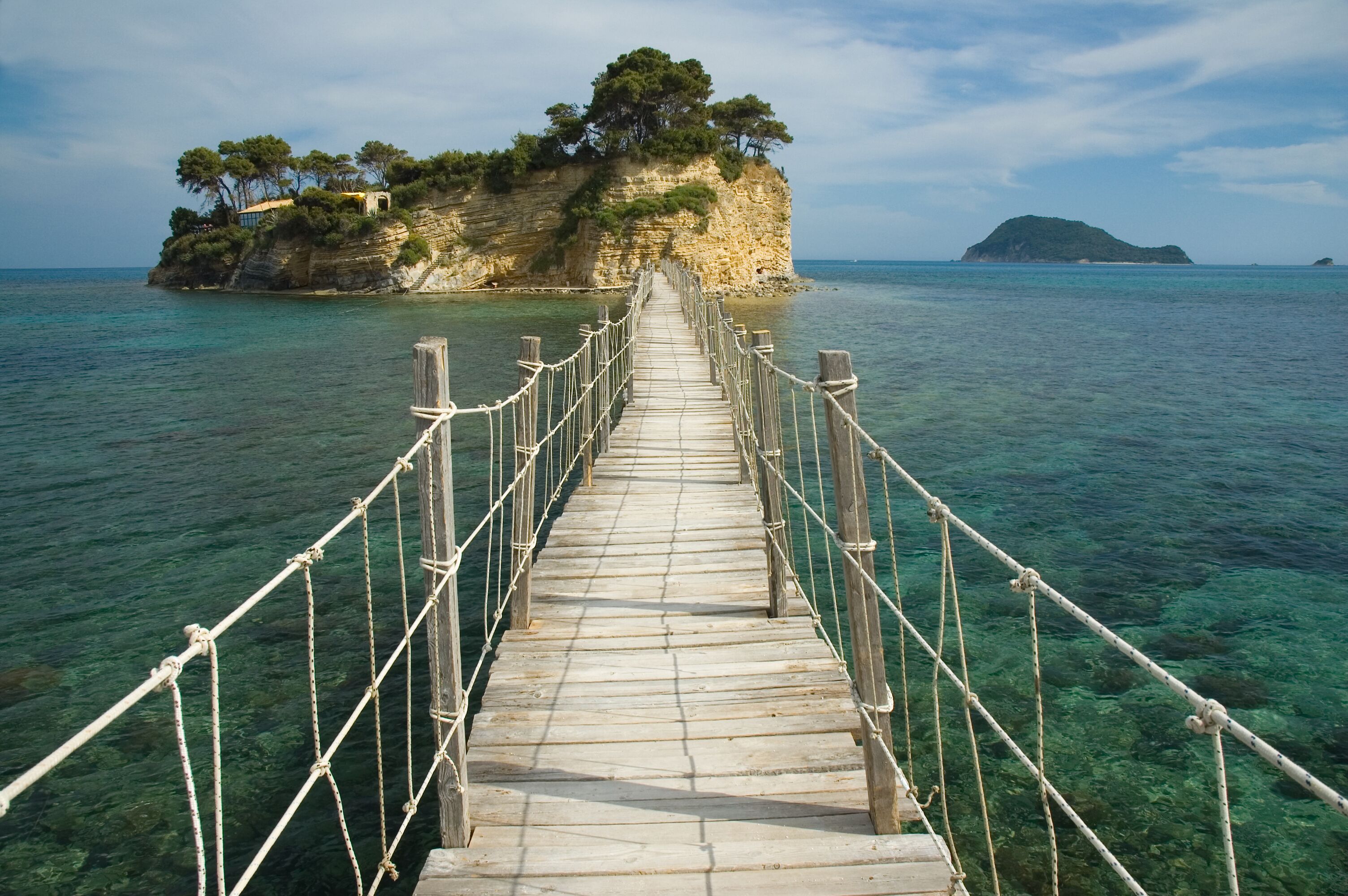 A wooden bridge leading to a rocky island with trees.