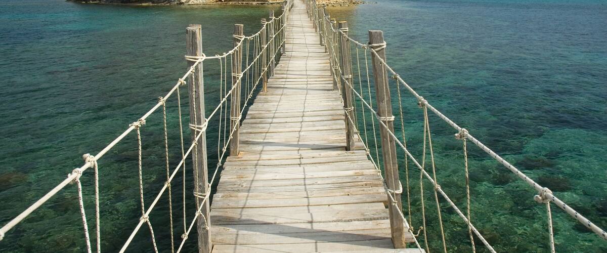 A wooden bridge leading to a rocky island with trees.