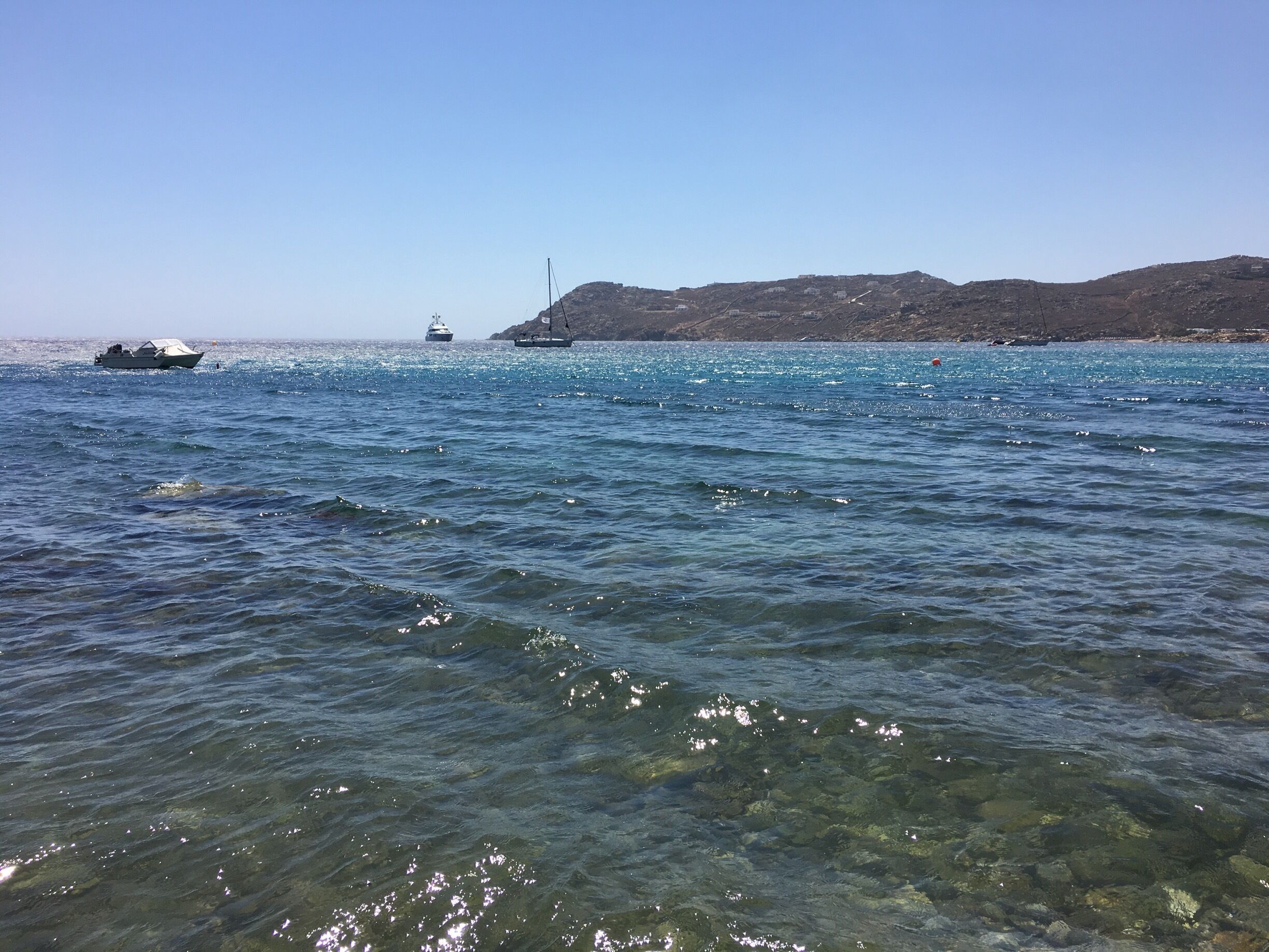 A clear coastal waterway with boats, rocky hills in the background, and a clear sky.