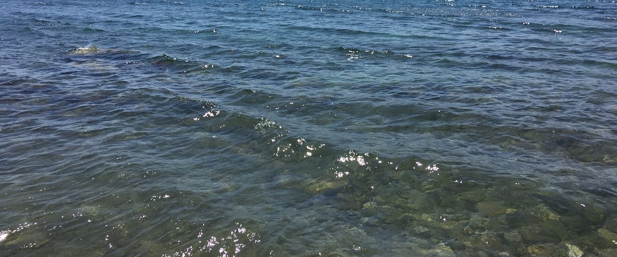 A clear coastal waterway with boats, rocky hills in the background, and a clear sky.