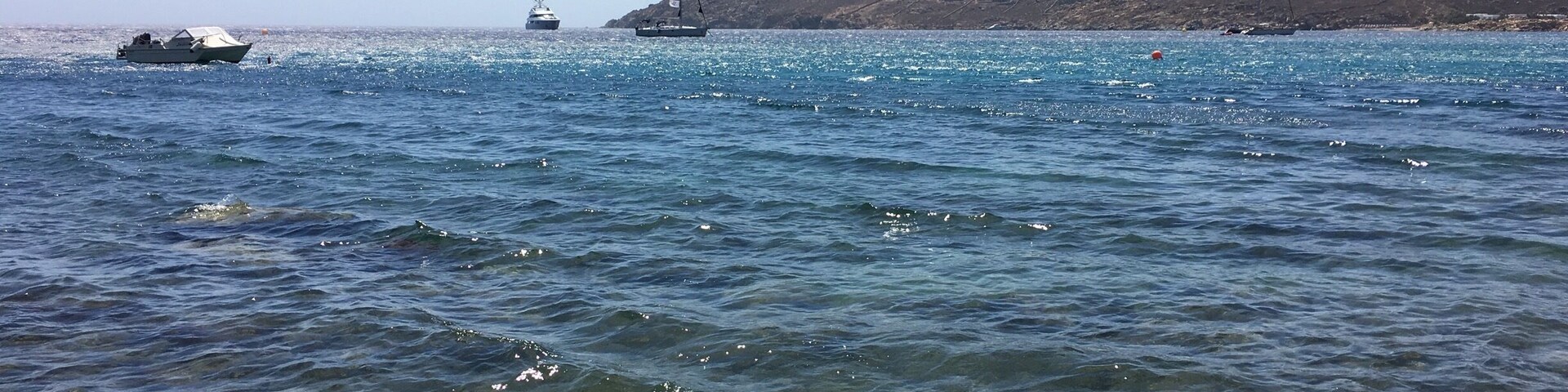 A clear coastal waterway with boats, rocky hills in the background, and a clear sky.