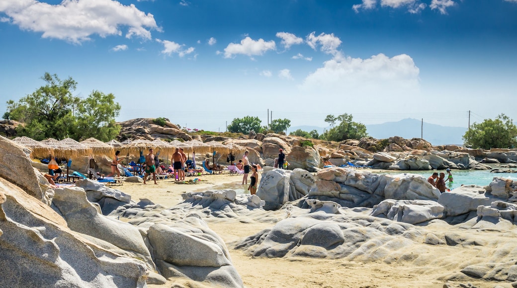 Een rotsachtig strand met rieten parasols en mensen die zonnebaden.