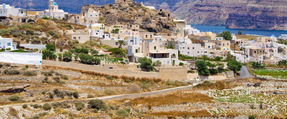 A coastal village with white buildings, a church with a blue dome, and a rocky cliff by the sea.
