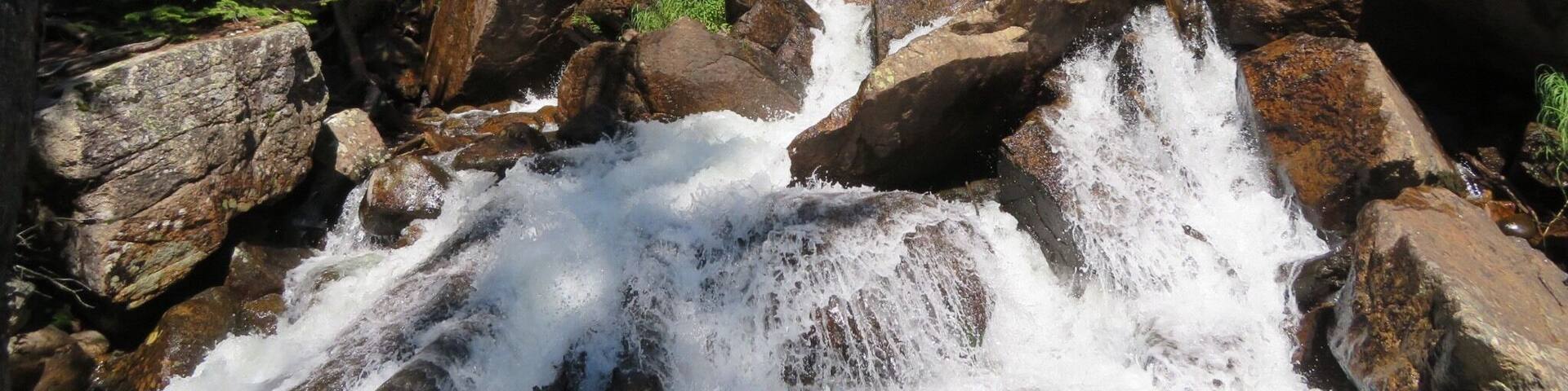 A waterfall cascading over large rocks surrounded by trees.