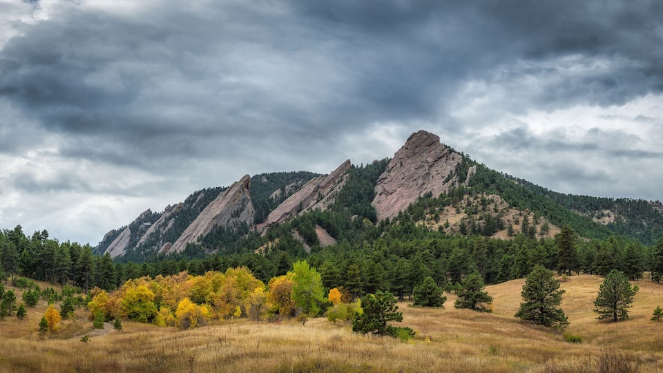 A mountain range with autumn foliage and a cloudy sky.