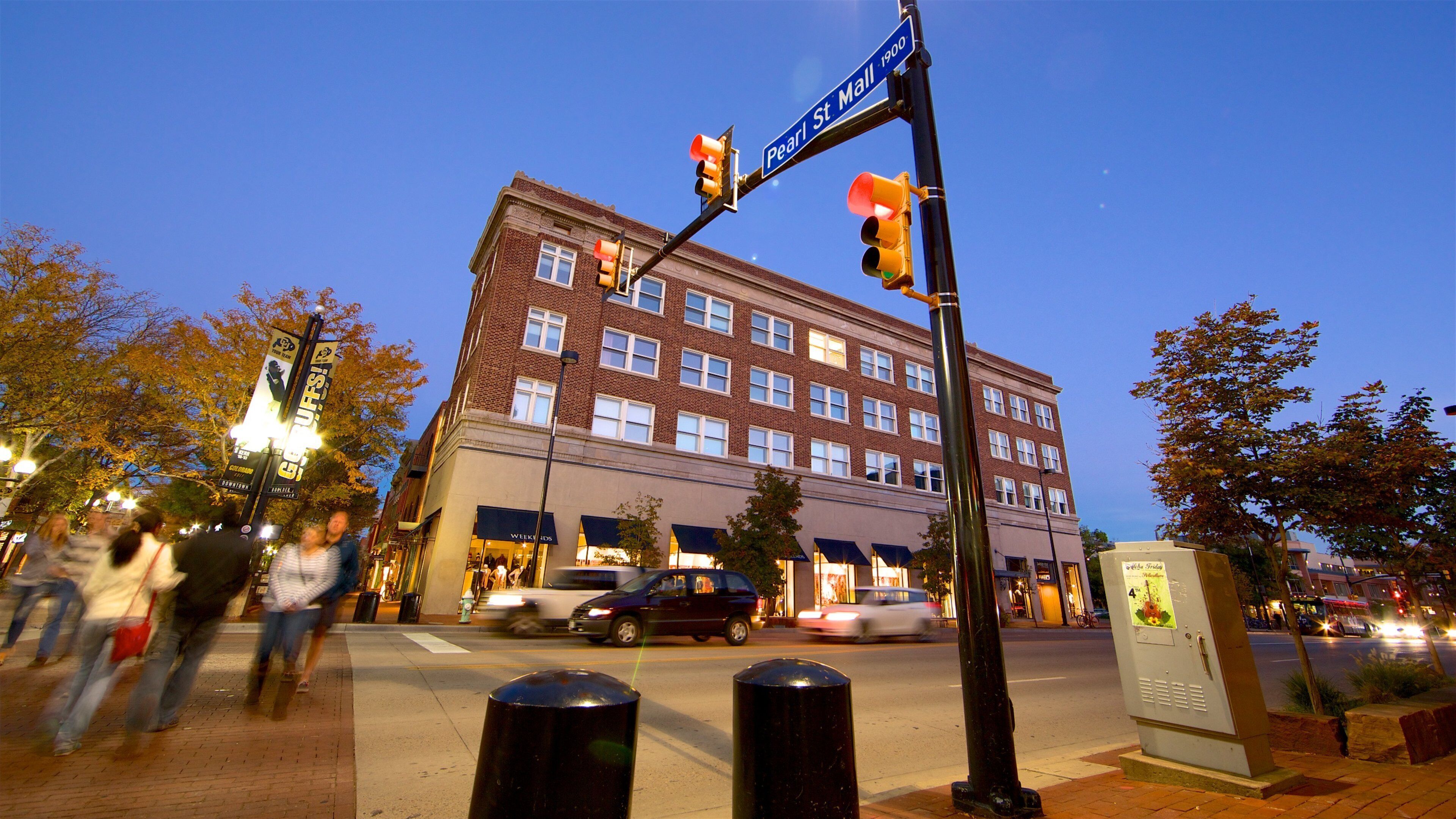 A street corner with a traffic light, a street sign reading "Pearl St Mall 1900", and a brick building with multiple windows.